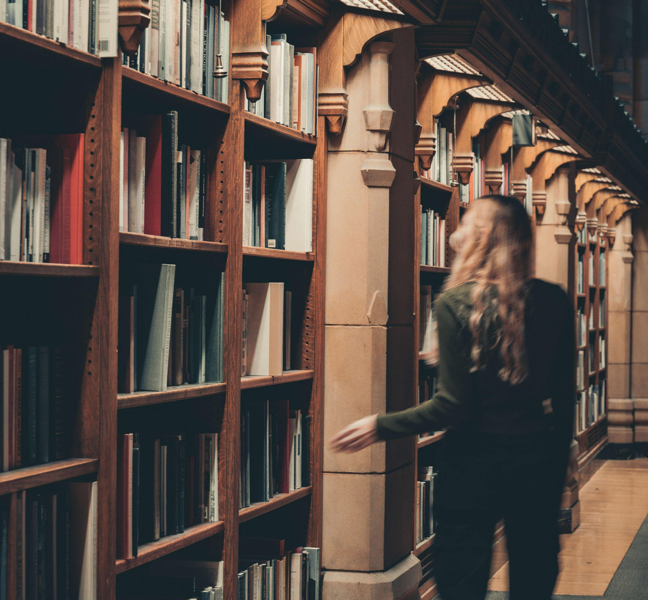 Iris A. Library Browsing A woman walks alongside bookshelves in a library. Her back is to the camera. Photo credit to: https://www.instagram.com/hello_meagain/